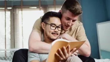 Two people reading a book together on the couch.