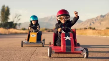 Two kids racing in soapbox cars on a sunny day.