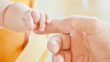 Baby hand holding an adult's finger gently.