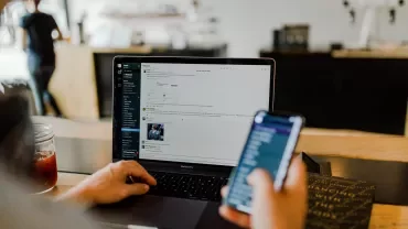 Persoon werkt op laptop en smartphone in een café.