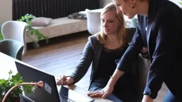 Twee mensen werken samen aan een laptop in een kantooromgeving.