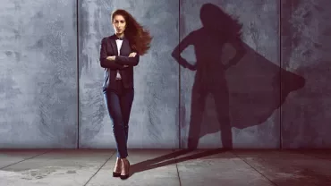 Person in suit stands with superhero shadow on wall.