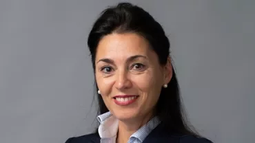 A smiling person in a dark jacket against a gray background.