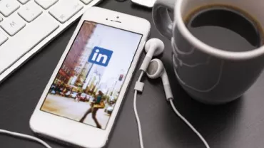 Een smartphone met de LinkedIn-app, naast een kop koffie en toetsenbord.