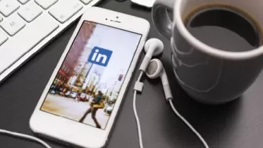 Een smartphone met de LinkedIn-app, naast een kop koffie en toetsenbord.