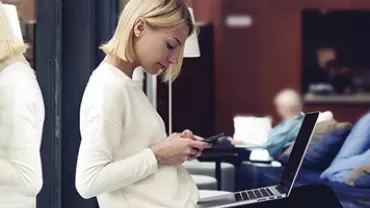 Persoon met laptop gebruikt een smartphone in een moderne ruimte.