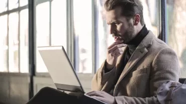 Person seated by a large window using a laptop.