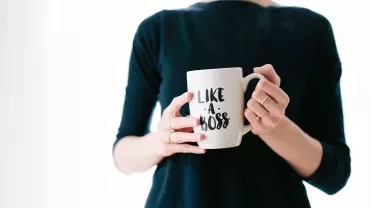Persoon houdt een mok vast met de tekst 'Like a Boss'.