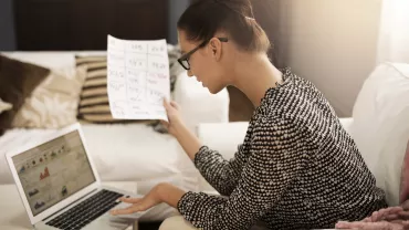 Person examining a document while working on a laptop.