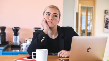 Persoon aan een tafel met een laptop, notitieboek en een kopje.