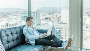 Person working on a laptop on a couch with city view.