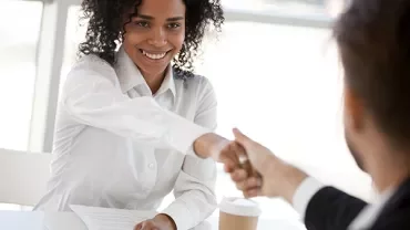 Individuals shaking hands across a table during a meeting.