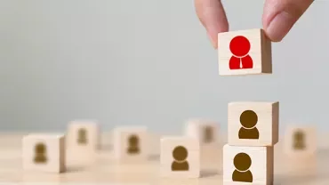 Hand legt houten blokken met mensfiguren op elkaar.
