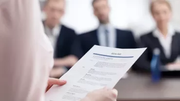 Persoon leest een cv tijdens een sollicitatiegesprek, met drie personen aan tafel.