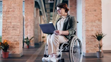 Persoon met een laptop in een rolstoel in een ruime gang.