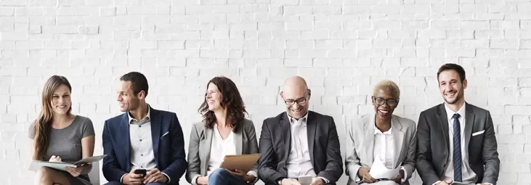 A group of people in business attire sitting against a brick wall.