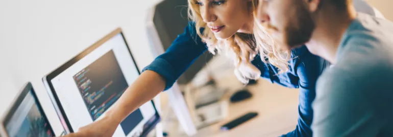 Collega's werken samen op een computer, wijzend naar het scherm.