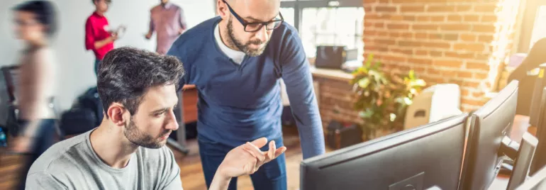 Twee mensen werken samen aan een computer in een modern kantoor.