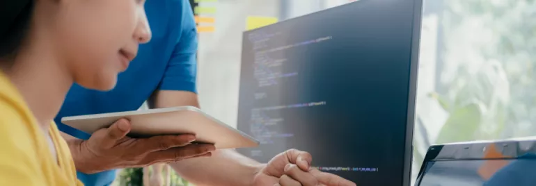 Twee mensen werken op een computer, één wijst naar het scherm.