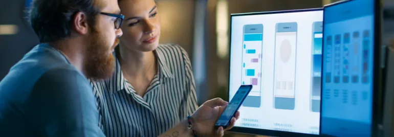 Twee personen werken aan mobiele app-ontwerp op een computerscherm.