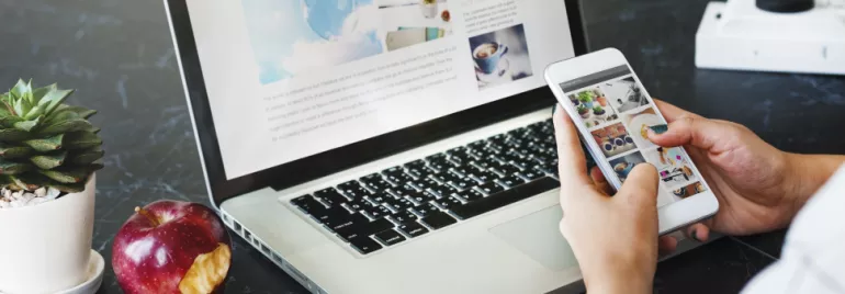 Iemand gebruikt een smartphone met een laptop op tafel.