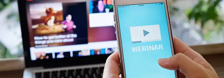 Telefoon toont webinar op scherm, laptop op achtergrond.