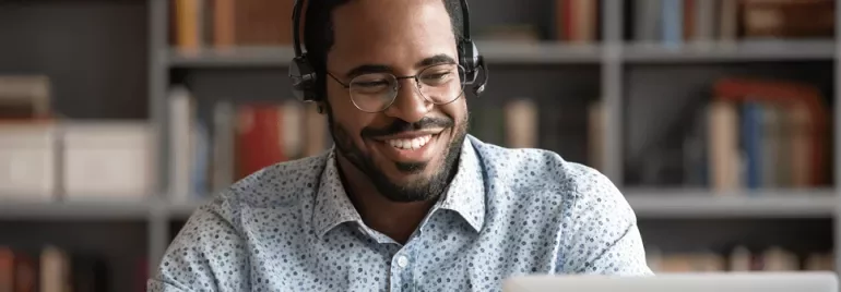 Persoon met een headset voor laptop, omringd door boeken in een kast.