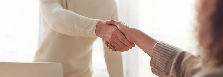 Twee mensen schudden elkaar de hand bij een bureau.