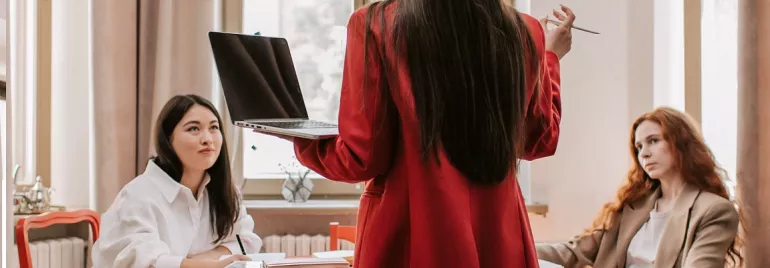 Person with laptop leading a discussion at a table in an office.
