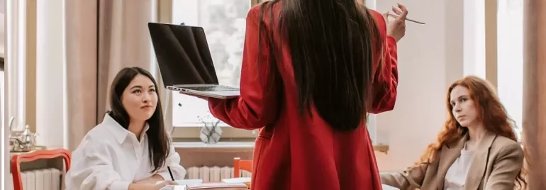 Person with laptop leading a discussion at a table in an office.