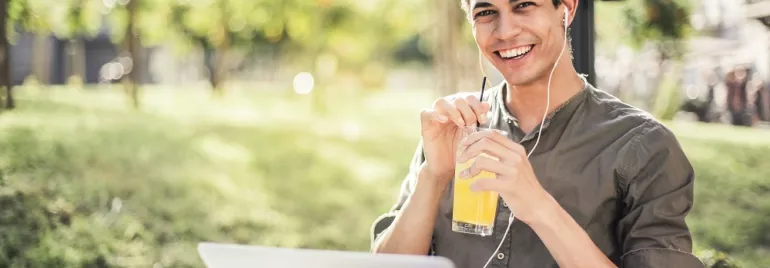 Man drinkt sap terwijl hij met een laptop buiten zit.