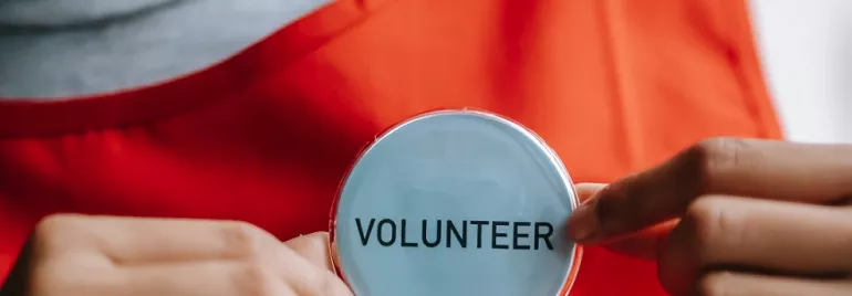 Persoon met vrijwilliger badge en oranje schort.