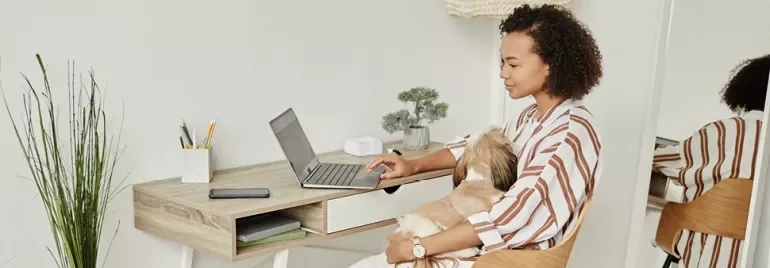 Persoon werkt aan laptop terwijl een hond op schoot ligt.