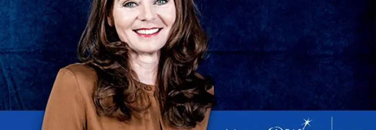 Person smiling against Make-A-Wish Netherlands backdrop.