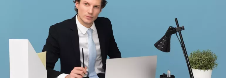 Persoon achter bureau met laptop en notitieblok, blauwe achtergrond.