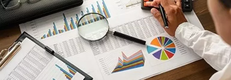 Person analyzing charts and using a calculator at a desk.