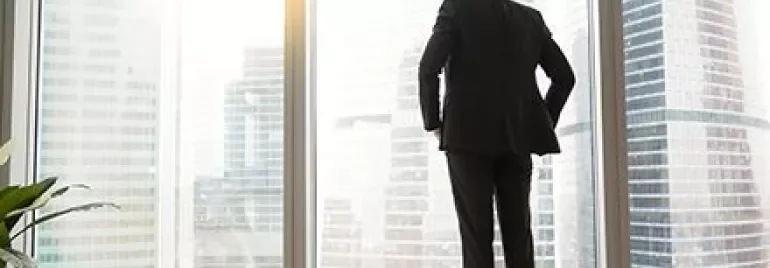 Persoon kijkt uit een raam naar stadse skyline bij daglicht.