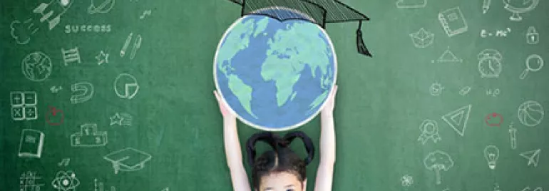 Child holds globe in front of chalkboard with educational drawings.