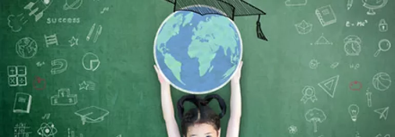 Child holds globe in front of chalkboard with educational drawings.