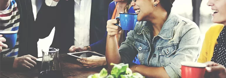 Groep mensen aan het genieten van koffie en lachen samen aan tafel.