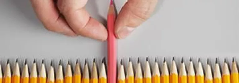 Hand picking a pink pencil from a line of yellow pencils.