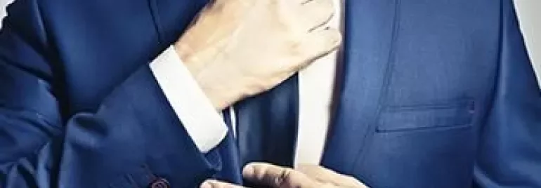 Person adjusting a tie on a blue suit.