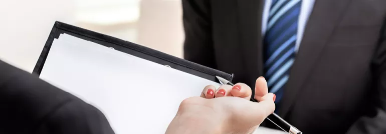 Een persoon geeft een pen en documenten aan een ander tijdens een gesprek.