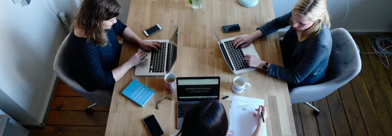 Three people collaborating at a table with laptops and coffee.