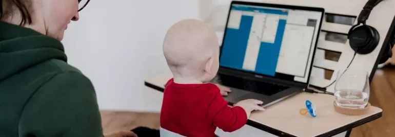 Volwassene met kind op schoot, kijkend naar een laptop.