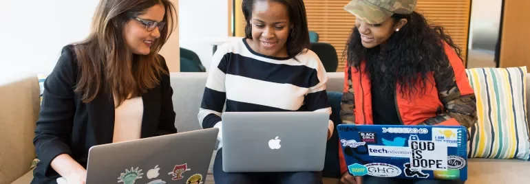 Three people collaborating with laptops on a couch.