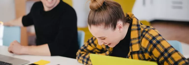 Twee mensen lachen samen terwijl ze met laptops werken.