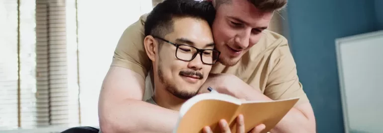 Two people reading a book together on the couch.