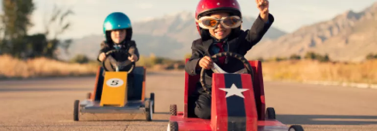 Two kids racing in soapbox cars on a sunny day.