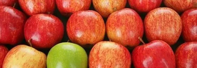 Rij rode appels met één groene appel ertussen.
